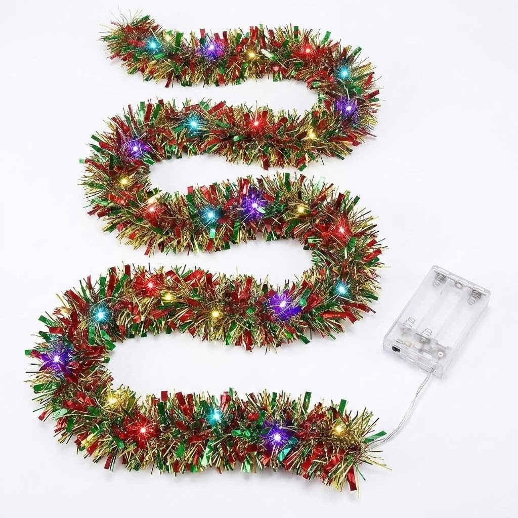 A red, green, and gold tinsel lighted garland forms winding rows on a white background beside an empty clear battery box.