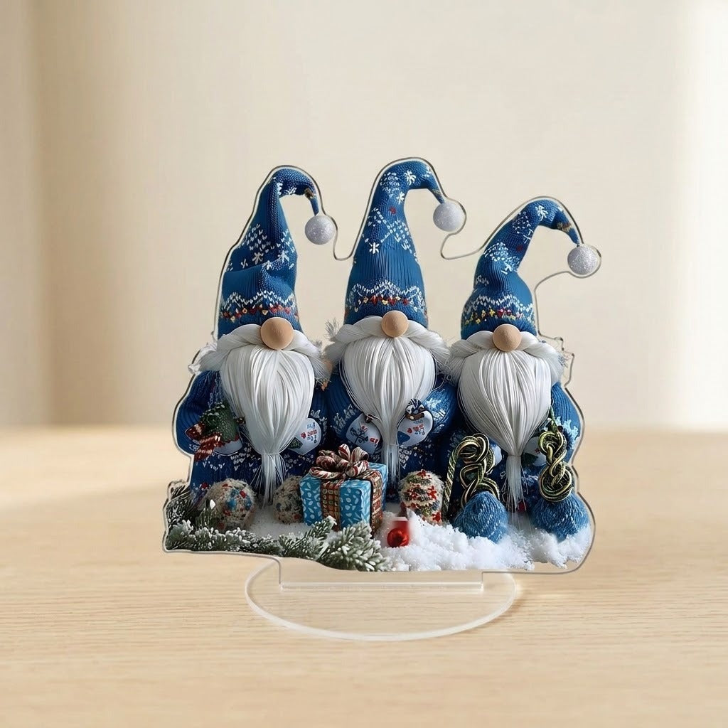 Acrylic tabletop decoration featuring three blue-hatted Christmas gnomes stands on a clear oval base on pale wood against a beige background.