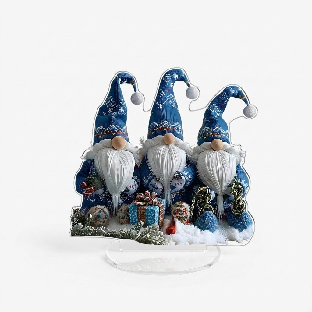 Acrylic tabletop decoration with three blue-hatted gnomes, white beards, and printed gifts stands on a clear oval base against white.