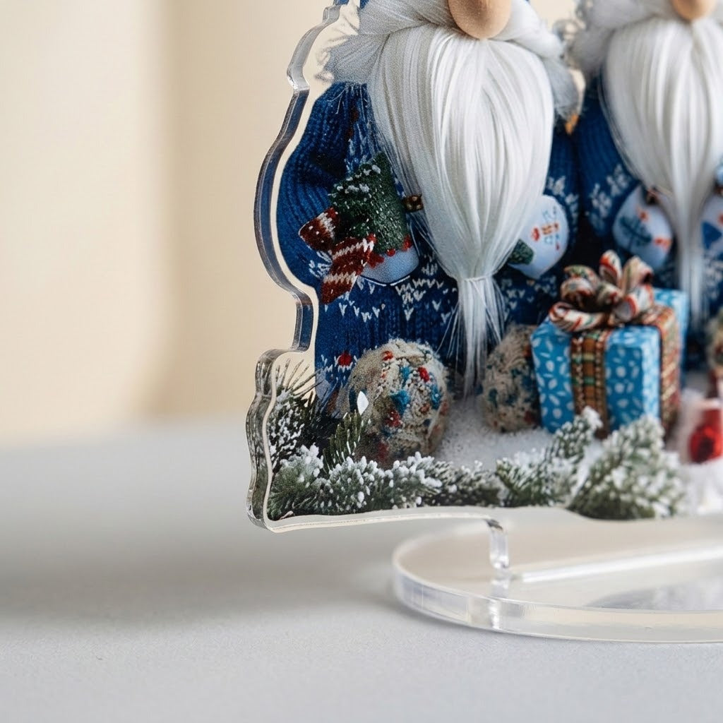 Close-up of the acrylic tabletop decoration shows its clear panel edge, printed blue gnomes, snowy greenery, and oval base against beige.