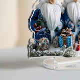 Close-up of the acrylic tabletop decoration shows its clear panel edge, printed blue gnomes, snowy greenery, and oval base against beige.
