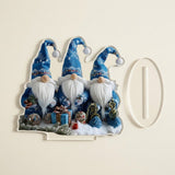 Acrylic tabletop decoration printed with three blue-hatted gnomes lies flat beside its detached clear oval slotted base on a cream background.