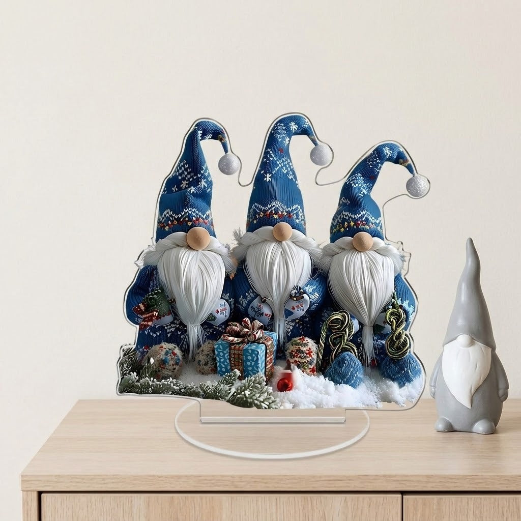 Blue Christmas gnome acrylic tabletop decoration on a clear base sits on a wooden cabinet beside a gray figurine against a cream wall.