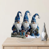 Blue Christmas gnome acrylic tabletop decoration on a clear base sits on a wooden cabinet beside a gray figurine against a cream wall.