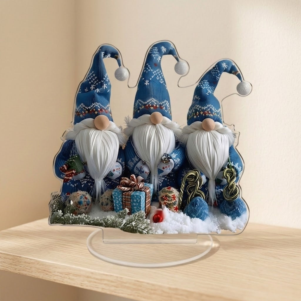 Acrylic tabletop decoration featuring three blue-hatted Christmas gnomes stands on a clear oval base on a wooden shelf against beige walls.