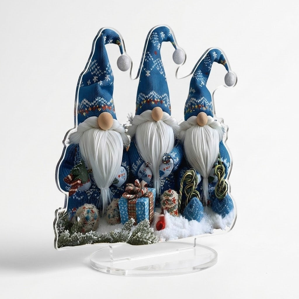 Angled acrylic tabletop decoration shows three blue-hatted gnomes, printed gifts, and snowy branches above a clear oval base against white.