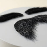 Black costume facial hair rests on a white surface, with mustache fibers in sharp focus and two matching eyebrows blurred behind.