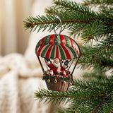 A timber Christmas ornament depicting Santa beneath a red, green, and cream striped canopy hangs from a pine branch against a blurred interior.
