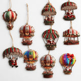 Ten timber Christmas ornaments with Santa balloon and parachute designs in festive stripes and rainbow colours hang from beige cords against white.