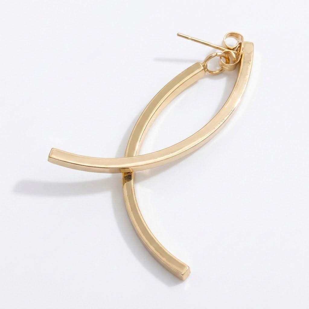 A gold-tone drop earring lies diagonally on white, with crossing curved bars, a connecting ring, and butterfly backing visible.