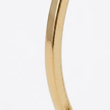 A close-up of a gold-tone drop earring shows its reflective curved bar and defined edges against white.