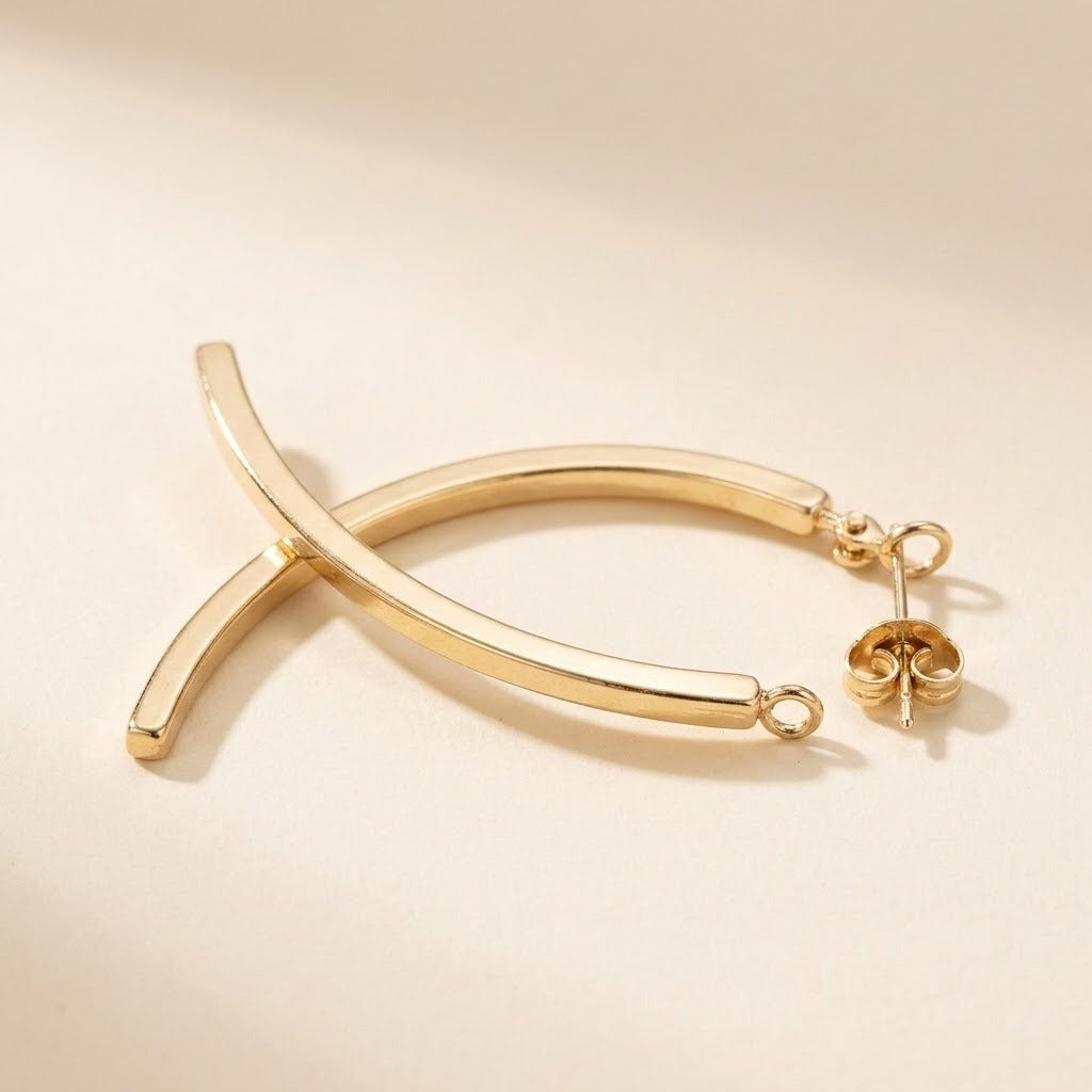 A gold-tone drop earring lies on a cream surface, showing crossing curved bars with its stud post and butterfly backing facing upward.