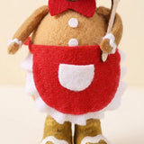 Close-up shows the tan plush gingerbread sitter’s red apron, white pocket, ruffled trim, white buttons, and spatula against a cream background.