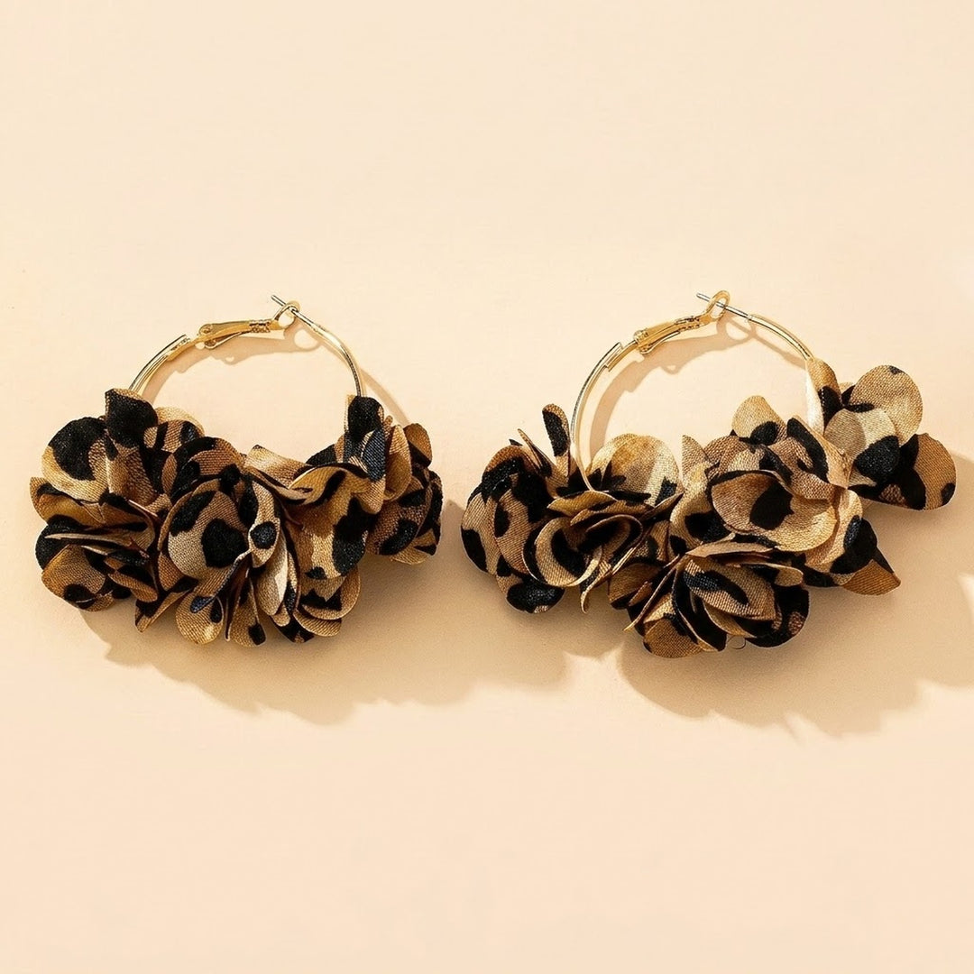 Two gold-tone hoop earrings with tan and black leopard-print fabric flower clusters lie side by side on a cream background.