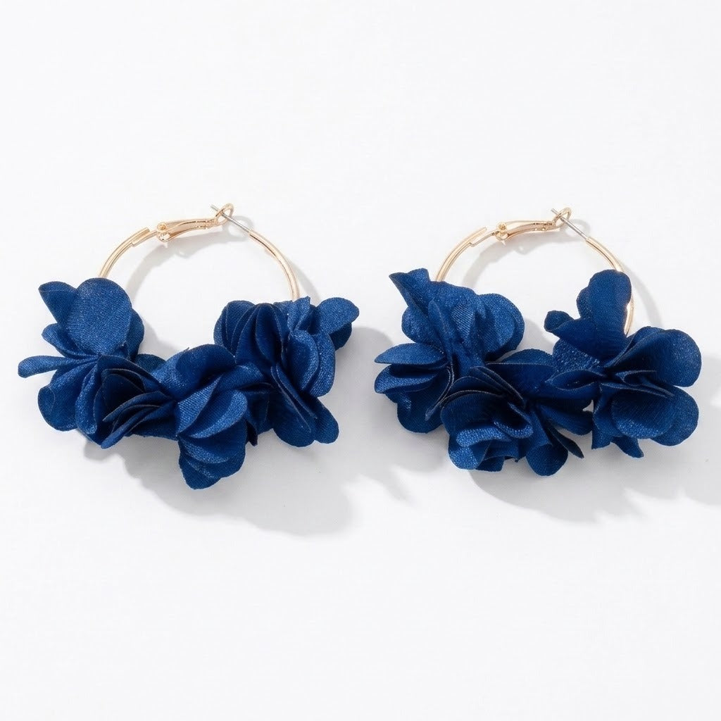 Two gold-tone hoop earrings with deep blue fabric flower clusters lie side by side on a white background.