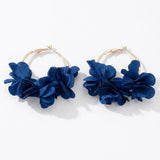 Two gold-tone hoop earrings with deep blue fabric flower clusters lie side by side on a white background.