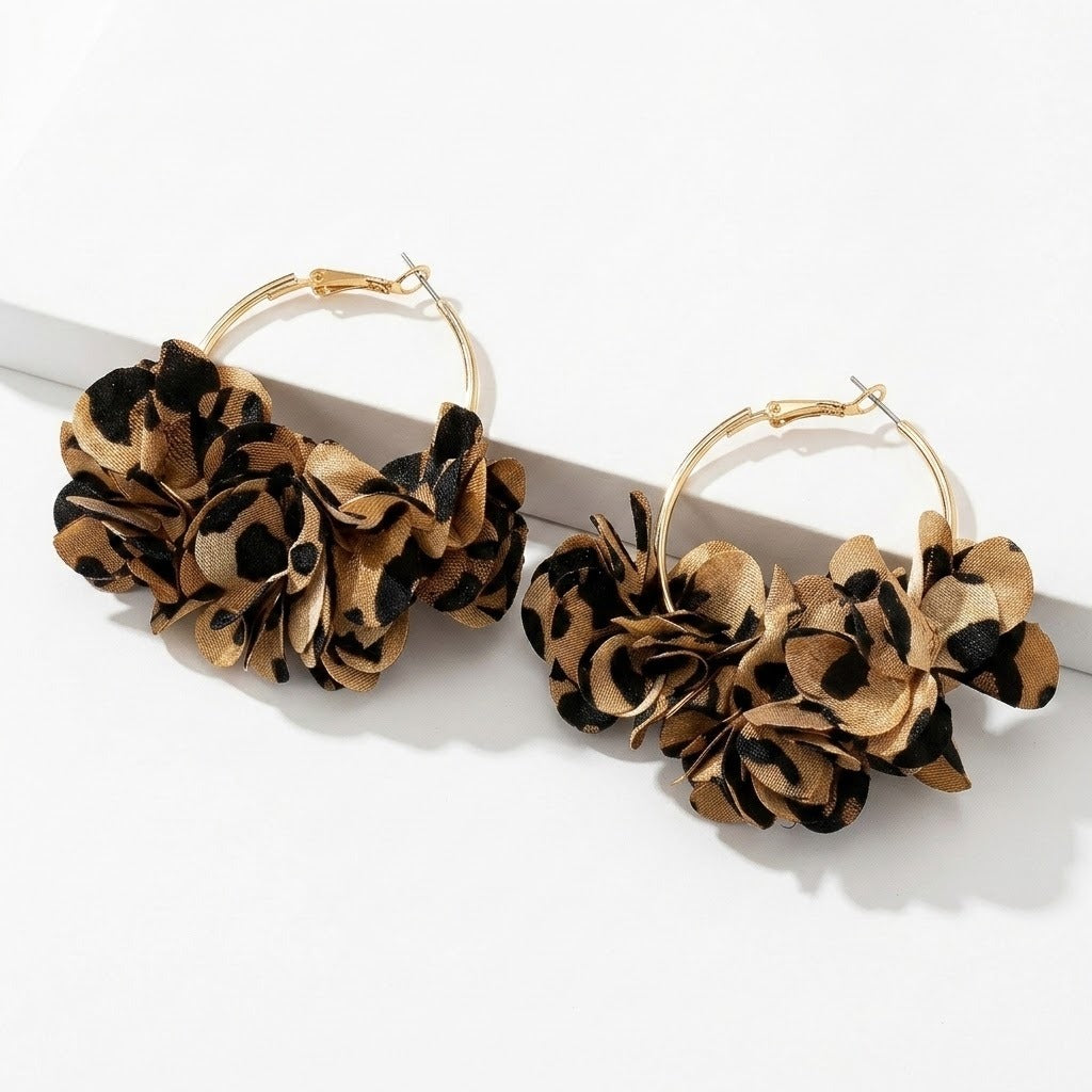 Two gold-tone hoop earrings with tan and black leopard-print fabric flower clusters rest against a white raised block.