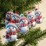 Six flat acrylic snowman Christmas ornaments with red patterned scarves hang from gold cords among green branches against a cream background.