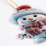 A flat acrylic snowman Christmas ornament with a clear edge, pale blue hat, and red plaid scarf rests against a white background.