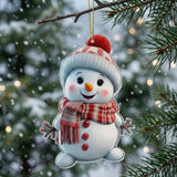 A flat acrylic snowman Christmas ornament with a red plaid scarf and pompom hat hangs against snowy greenery and blurred warm lights.