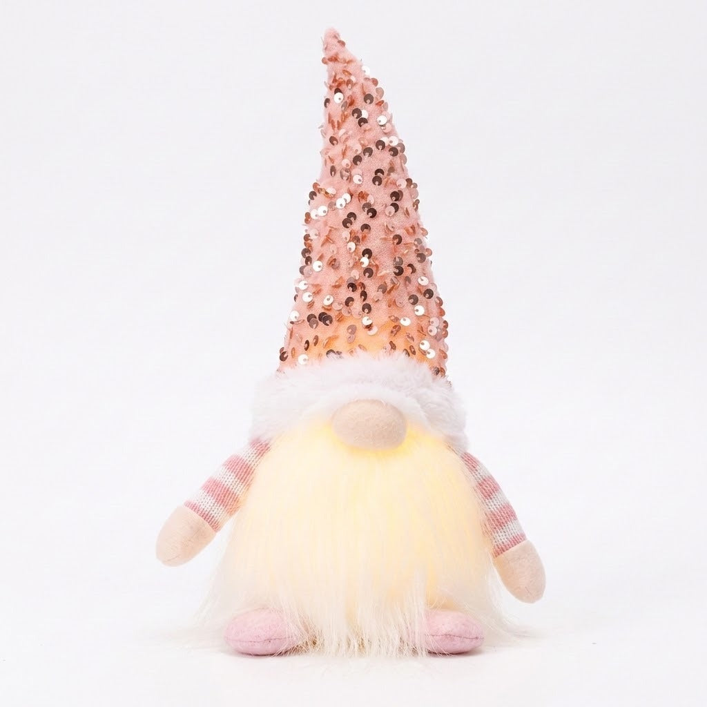 A Christmas gnome with a pink sequined hat, striped sleeves, pink feet, and glowing white beard stands against a white background.