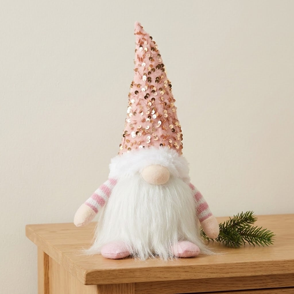 An unlit Christmas gnome with a pink sequined hat and white beard stands on a wooden cabinet beside an evergreen sprig.