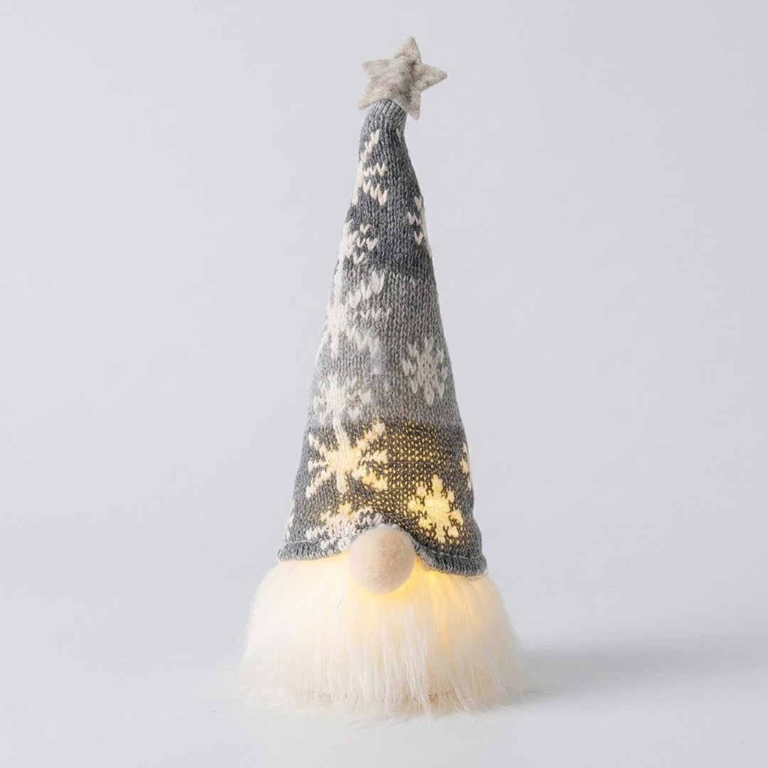Glowing Christmas gnome wears a gray knitted snowflake hat with a pale star above its white beard against a light gray background.