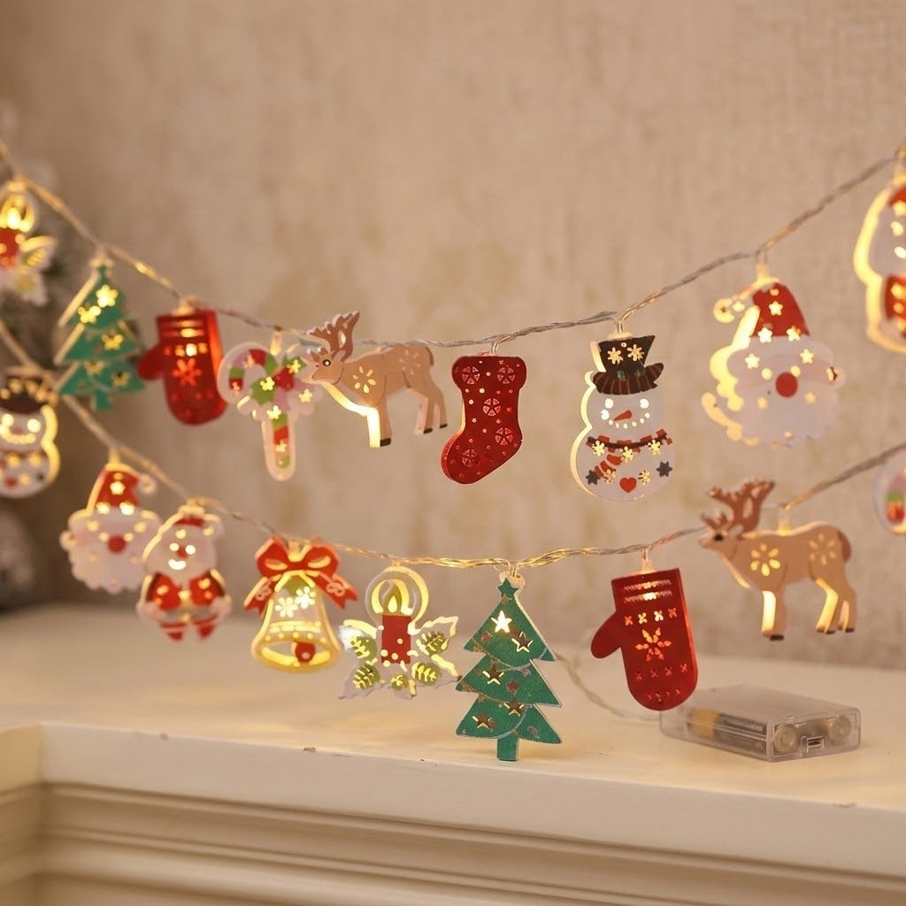 A warm white string light with colorful Christmas ornaments hangs above a white mantel beside a clear battery box.