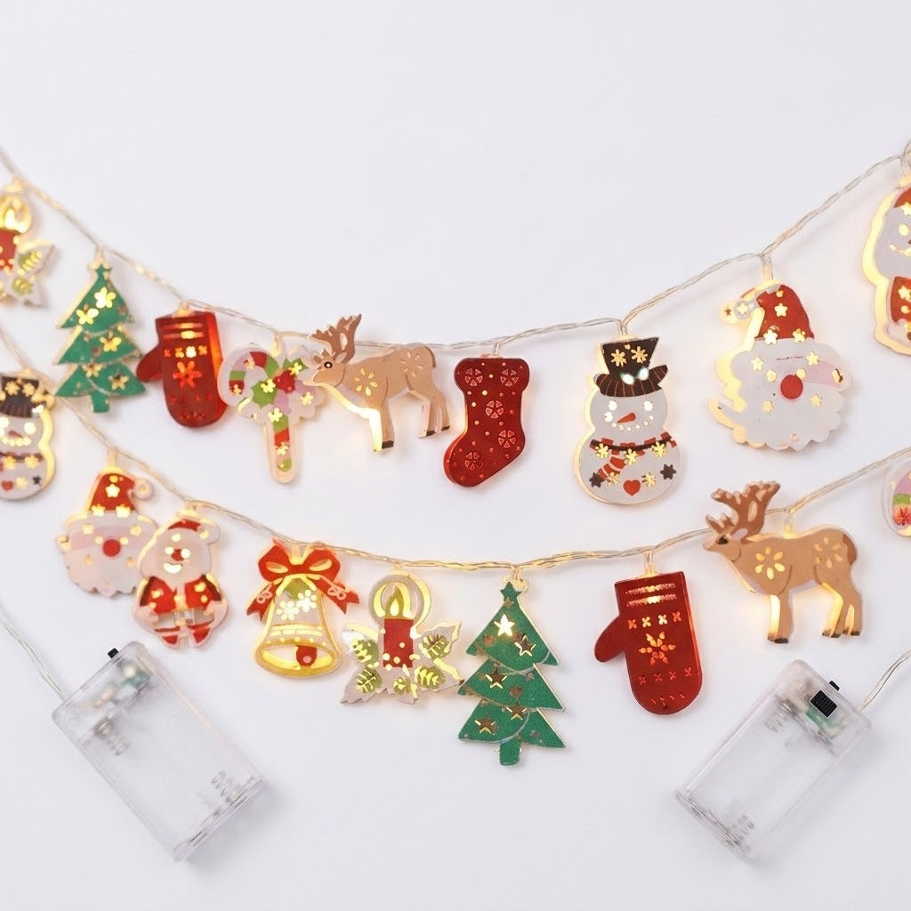 Two illuminated string light strands with red, green, white, and gold Christmas ornaments lie on a white background beside clear battery boxes.
