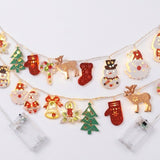 Two illuminated string light strands with red, green, white, and gold Christmas ornaments lie on a white background beside clear battery boxes.