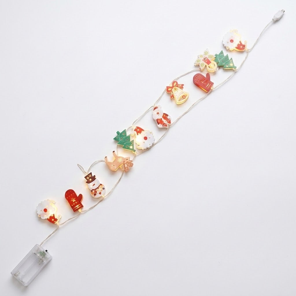 A string light with colorful Christmas ornaments lies diagonally on a white background, with a clear battery box at the lower left.