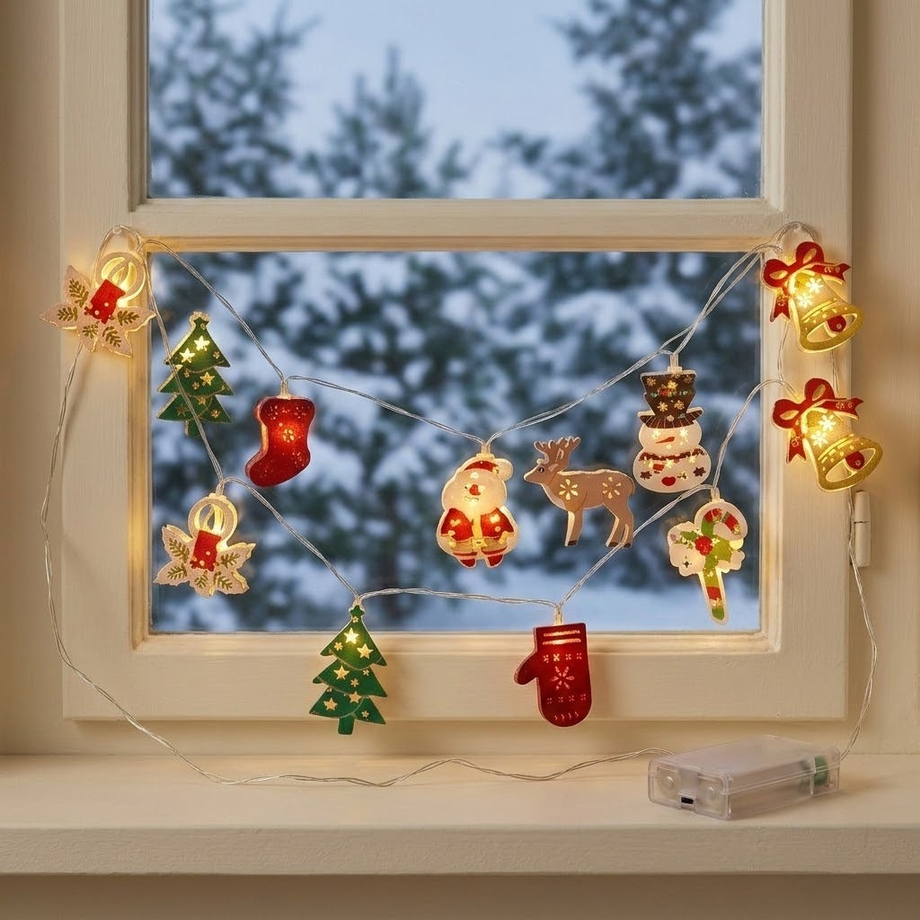 A glowing string light with colorful Christmas ornaments drapes across a white window overlooking snowy trees, with a clear battery box on the sill.