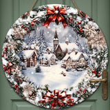 Round wood Christmas sign with flat snowy village artwork and red bows hangs by rope on a green paneled door.