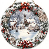 Round hanging Christmas sign depicting a snowy village, bordered by evergreen branches, red bows, berries, pinecones, and snowflakes against white.