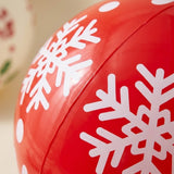 A close-up of the red PVC inflatable ornament shows white snowflakes and a raised panel seam against a blurred beige background.