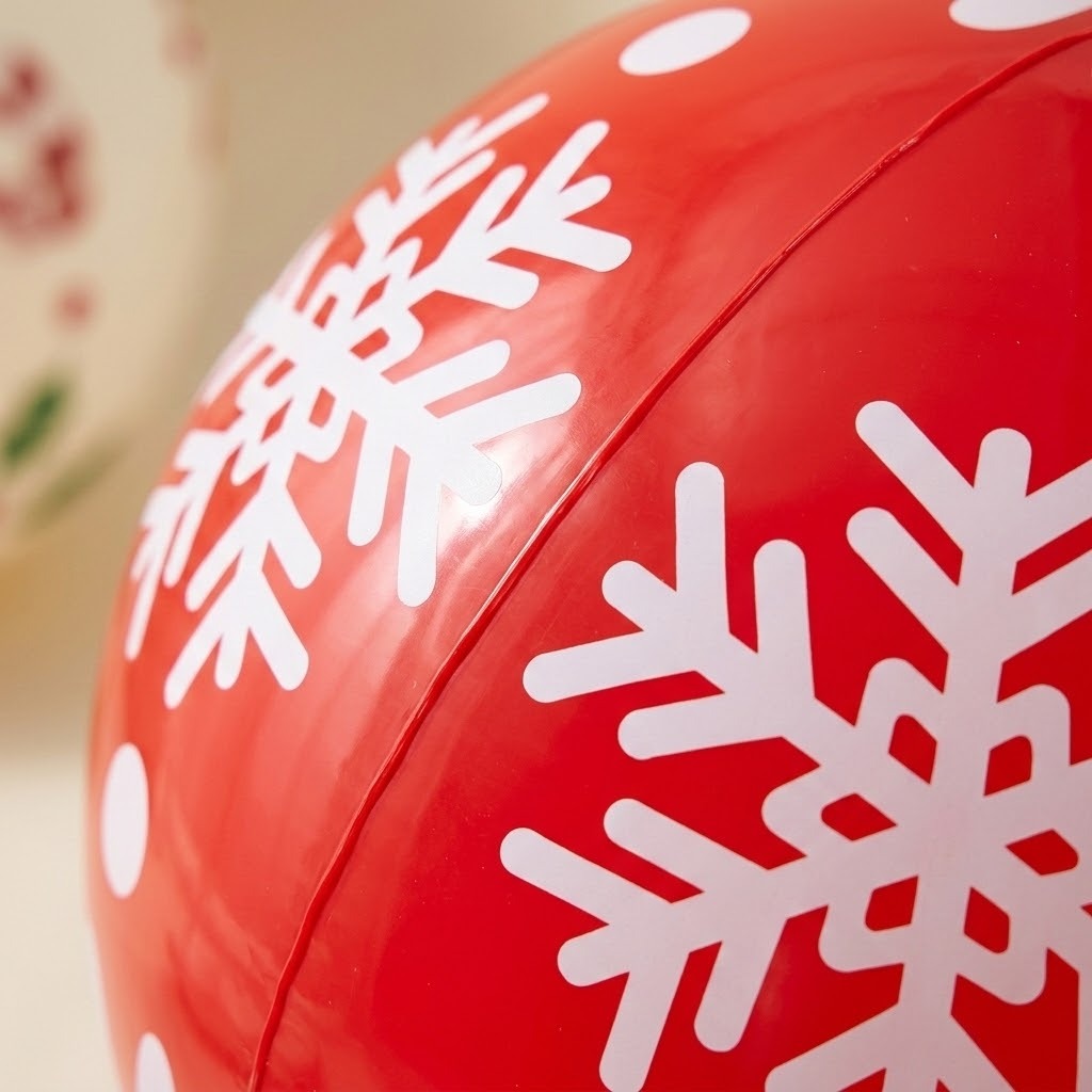 A close-up of the red PVC inflatable ornament shows white snowflakes and a raised panel seam against a blurred beige background.