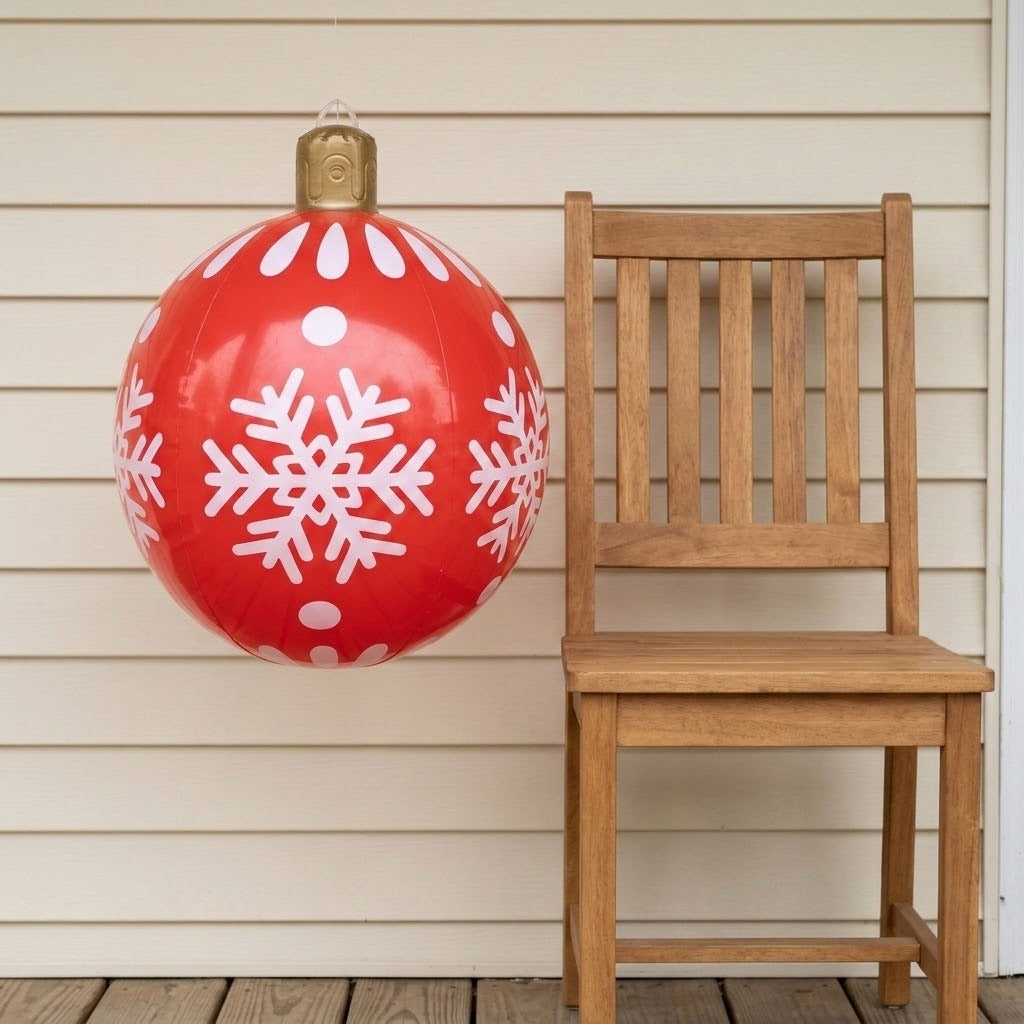 A red inflatable ornament with white snowflakes and a gold top hangs beside a wooden chair against cream porch siding.