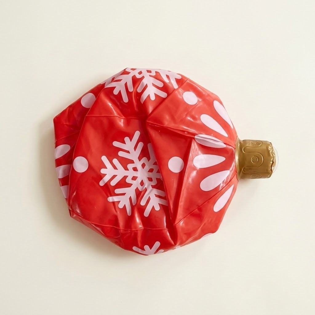 Deflated red inflatable ornament with white snowflakes and dots and a gold cap lies on an off-white background.