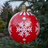 Red inflatable ornament with white snowflakes and dots and a gold hanging cap hangs from an evergreen branch outdoors.