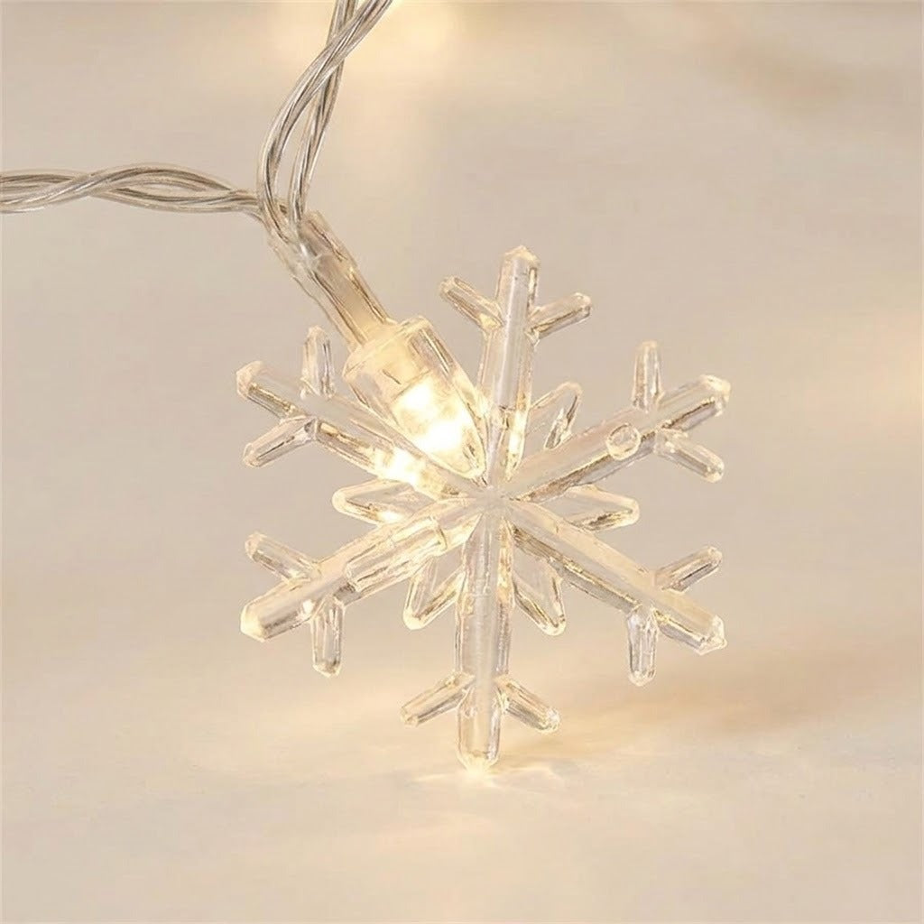 Clear plastic snowflake string lights glowing with a warm white light, shown close-up against a soft beige background.