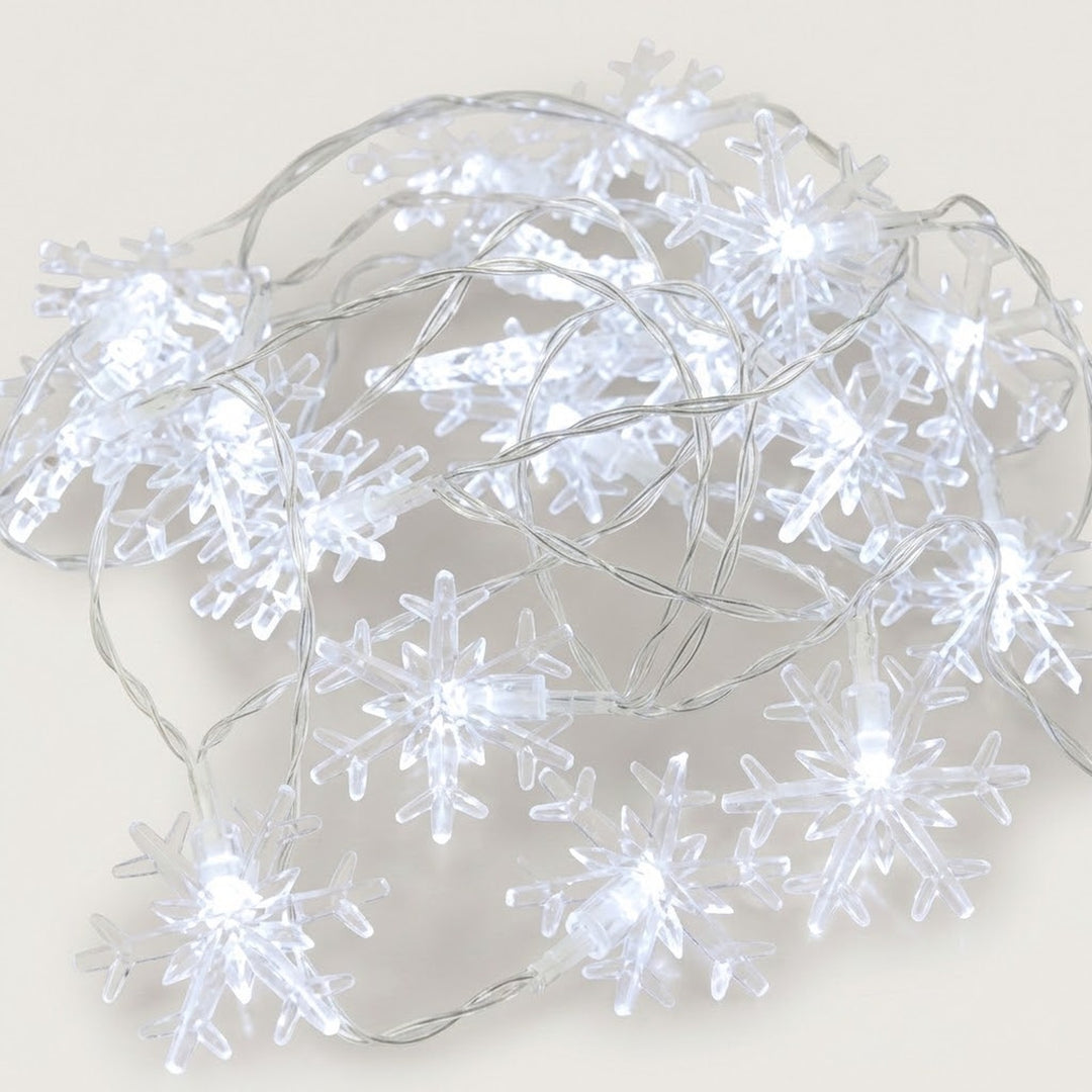 Cool white snowflake string lights with transparent snowflake covers and clear wires lie loosely coiled on a pale background.