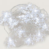 Cool white snowflake string lights with transparent snowflake covers and clear wires lie loosely coiled on a pale background.