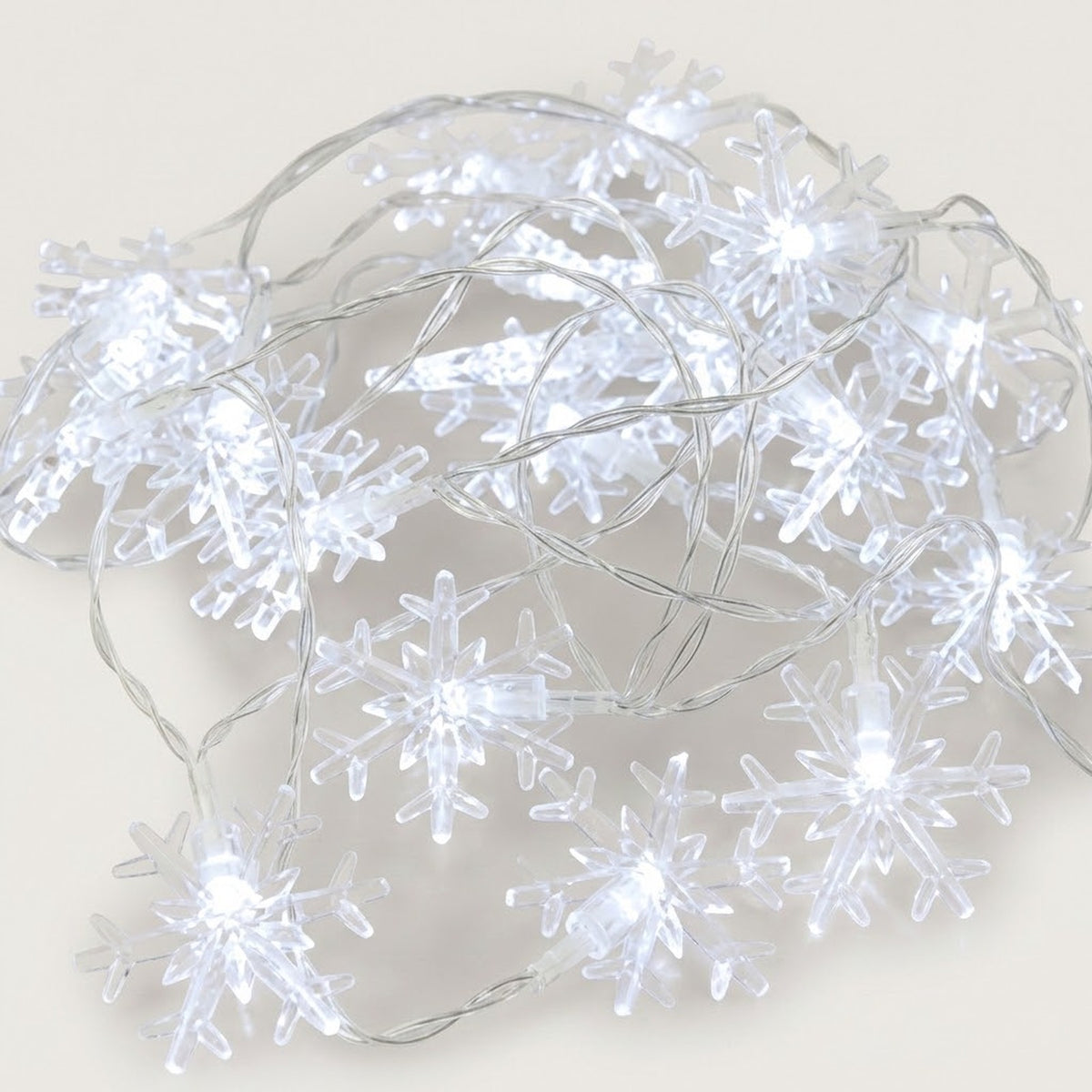 Cool white snowflake string lights with transparent snowflake covers and clear wires lie loosely coiled on a pale background.