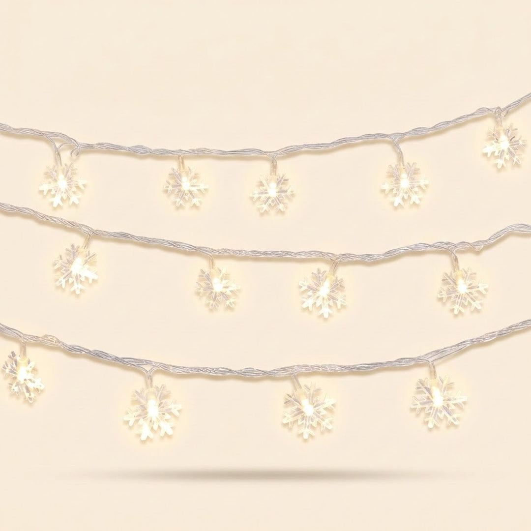 Warm white snowflake string lights hang in three curved rows on clear wire against a pale cream background.