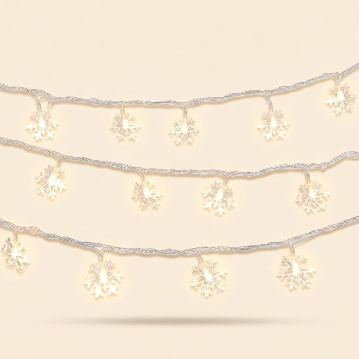 Warm white snowflake string lights hang in three curved rows on clear wire against a pale cream background.