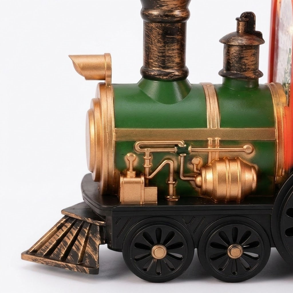 Christmas train decoration close-up shows a green boiler, gold-colored pipes, bronze-colored chimney, and black spoked wheels against a white background.