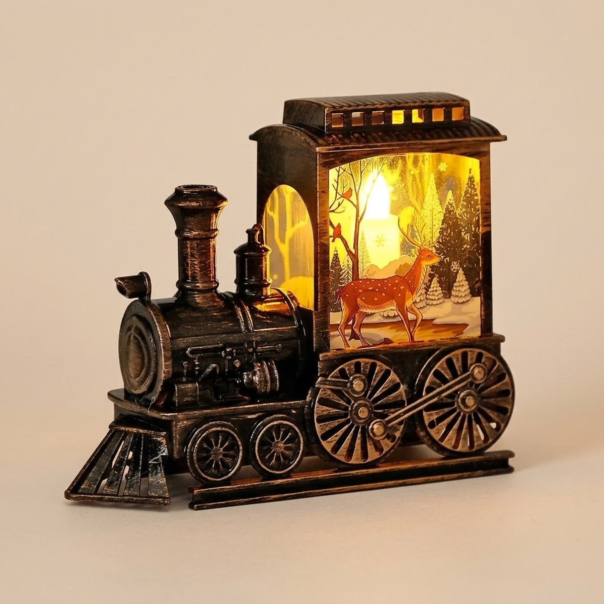 A bronze-tone decorative locomotive displays an illuminated deer and snowy forest illustration against a plain beige background.