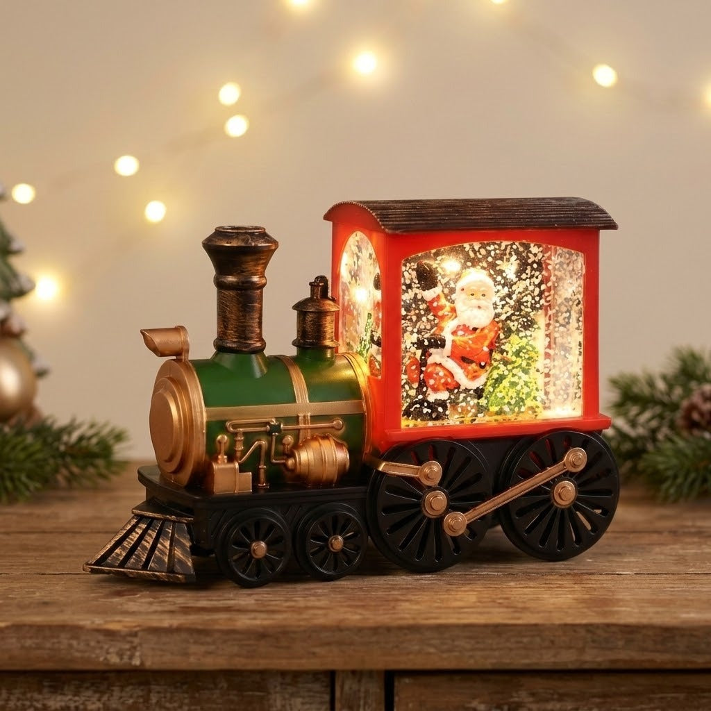 Red and green Christmas train decoration with a glowing Santa scene sits on a wooden cabinet beneath blurred string lights, beside evergreen sprigs.
