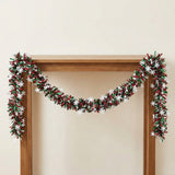 Red and green tinsel garland with white snowflakes drapes across a wooden frame against a cream wall.