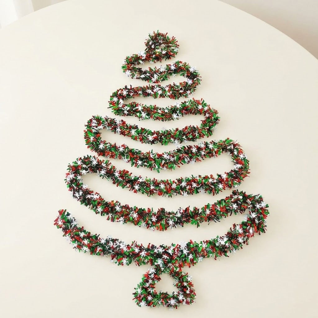 Red and green tinsel garland with white snowflakes forms a Christmas tree outline on a cream tabletop.